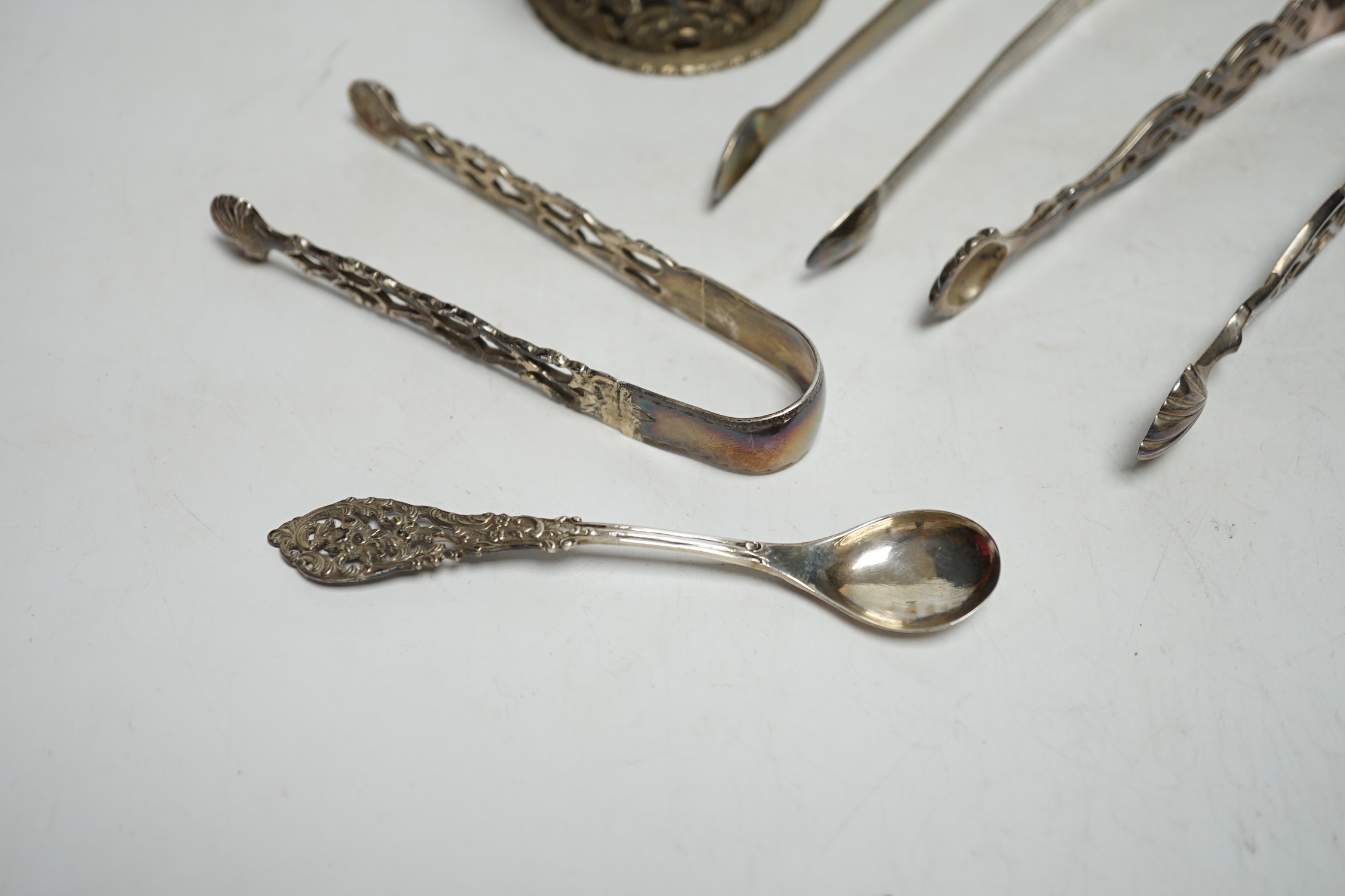 A Victorian silver embossed mustard pot, with spoon and three pairs of George III and later silver sugar tongs.
